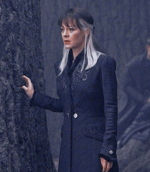 a woman with white hair standing next to a tree