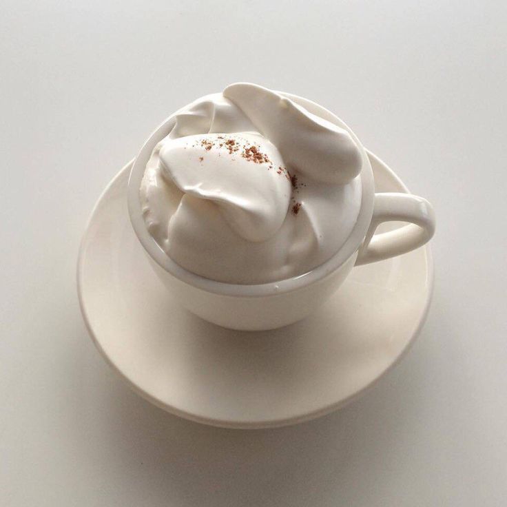 a white cup filled with whipped cream on top of a saucer