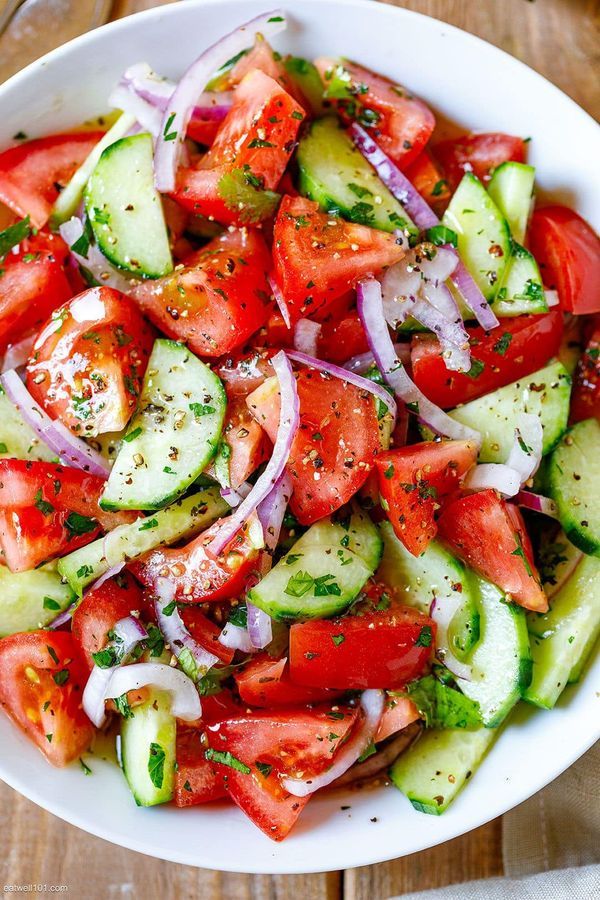 a white bowl filled with cucumber, tomato and onion salad on top of a wooden table