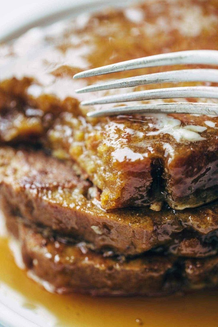 a stack of pancakes with syrup and a fork sticking out of the top on a white plate