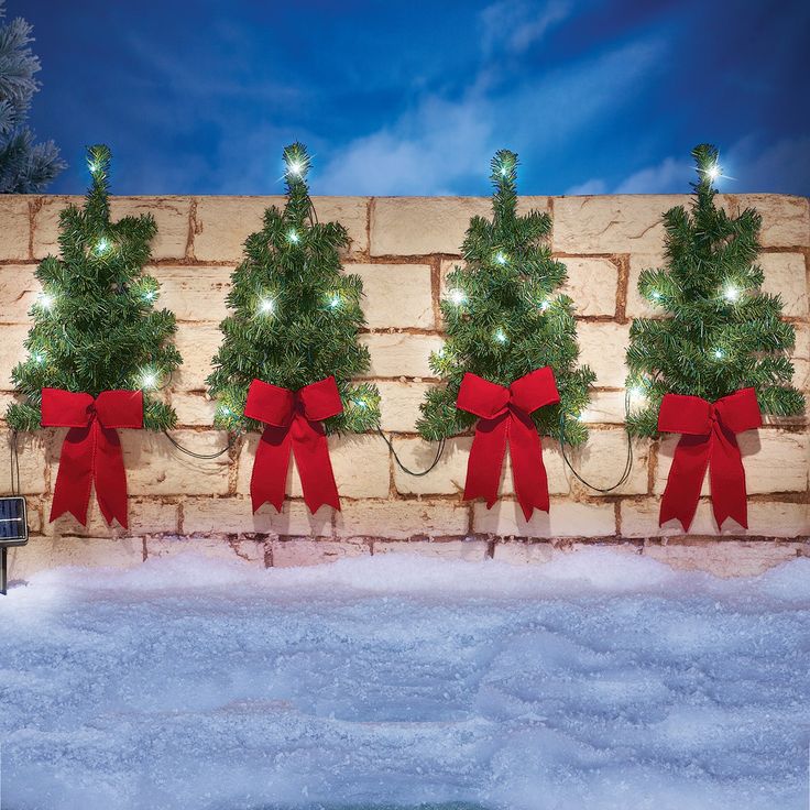 a brick wall decorated with christmas trees and red bows, surrounded by snow at night