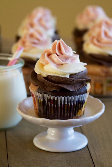 two cupcakes with frosting on a plate next to a glass of milk