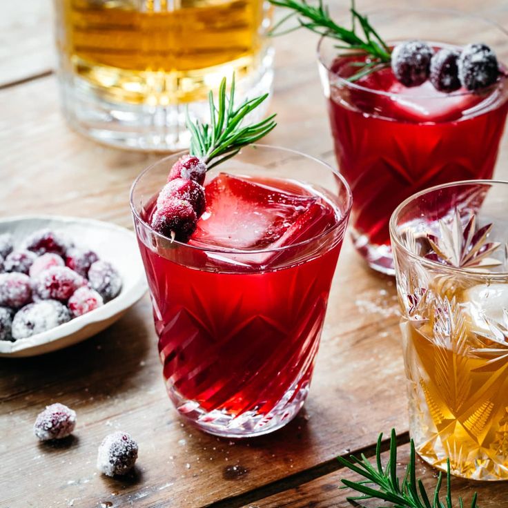 three glasses filled with different types of drinks on top of a wooden table next to plates