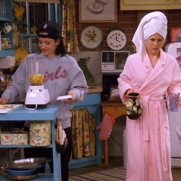 two women standing in a kitchen with one holding a blender and the other wearing a towel