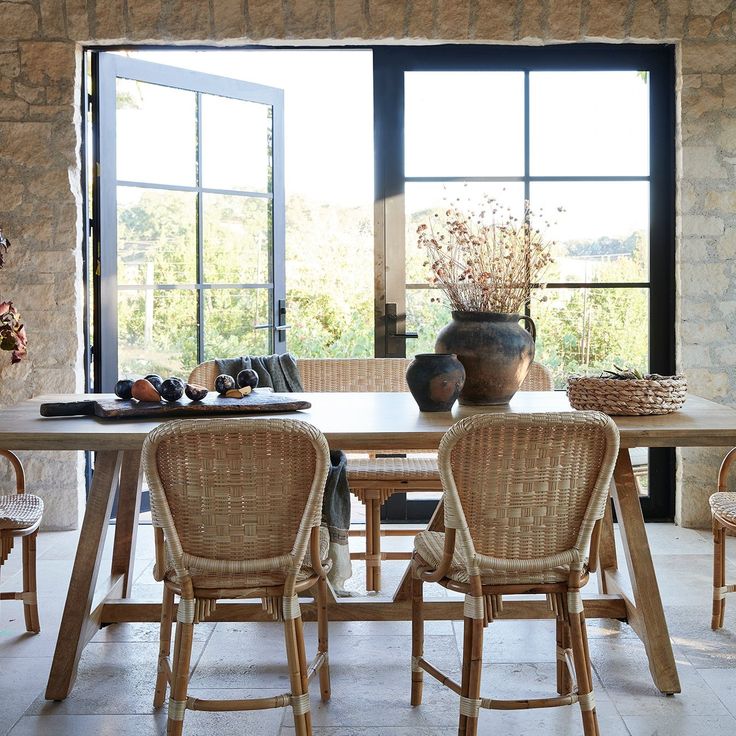 a dining room table with chairs and a vase on it's side, in front of a stone wall