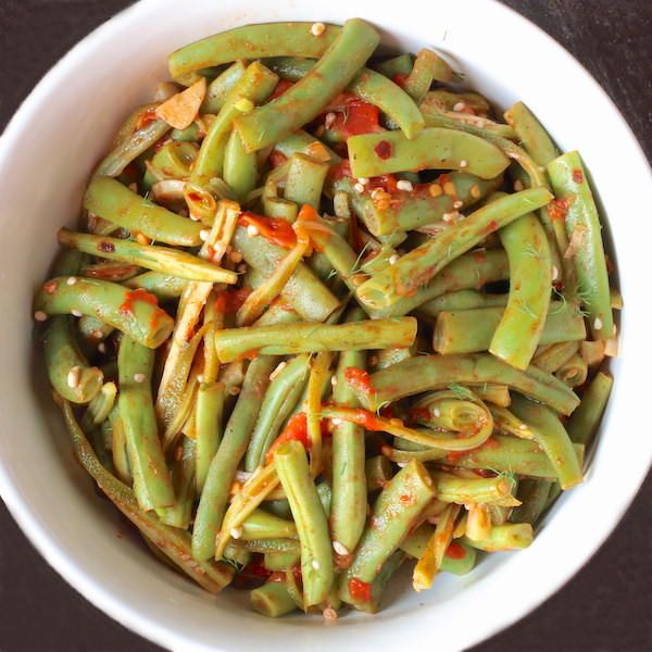 a white bowl filled with green beans covered in seasoning next to a black table