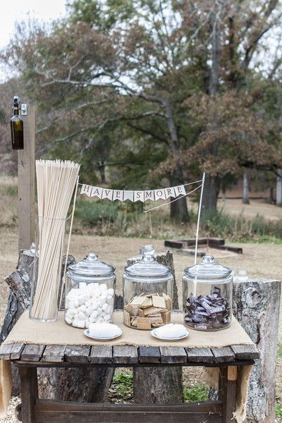 an outdoor picnic table with jars and marshmallows