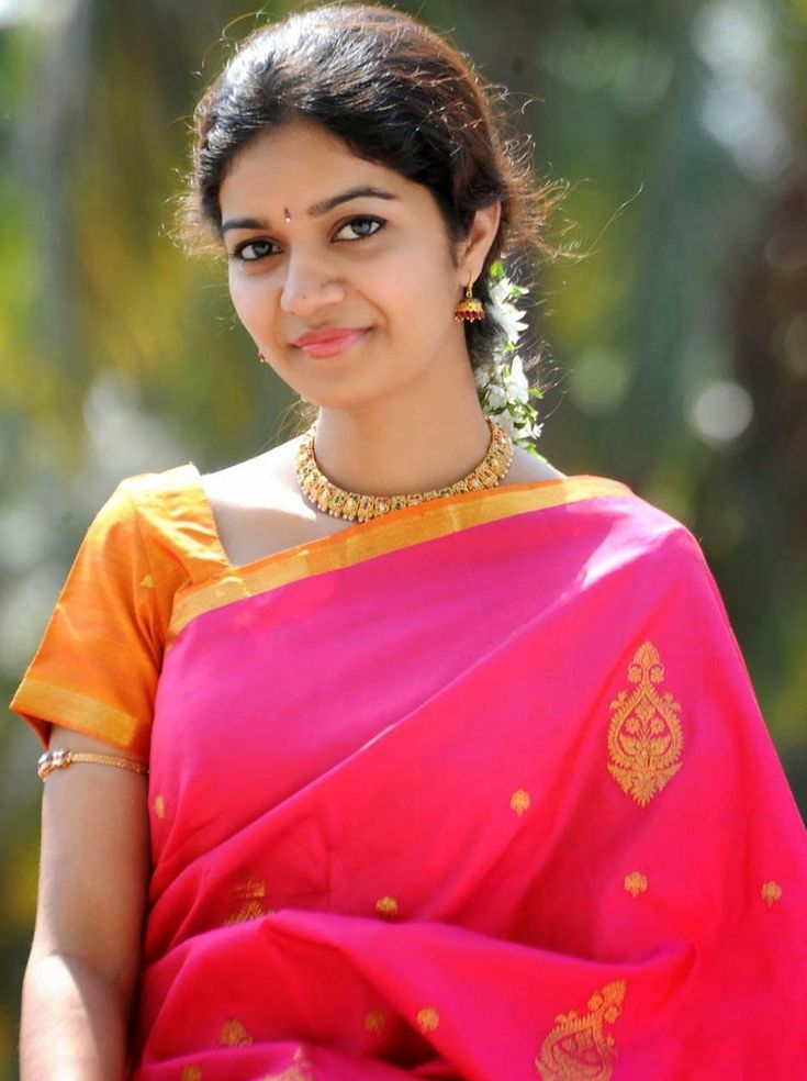 a woman in a pink sari with gold accents on her neck and shoulders, smiling at the camera