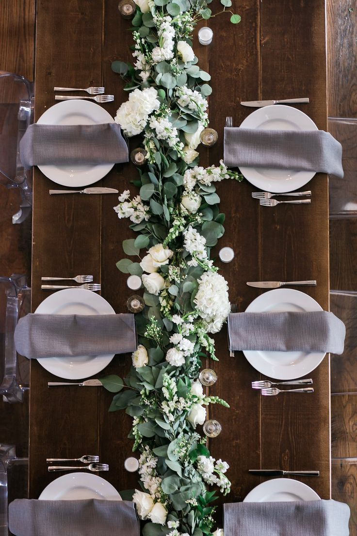 the table is set with plates and silverware, flowers and greenery on it