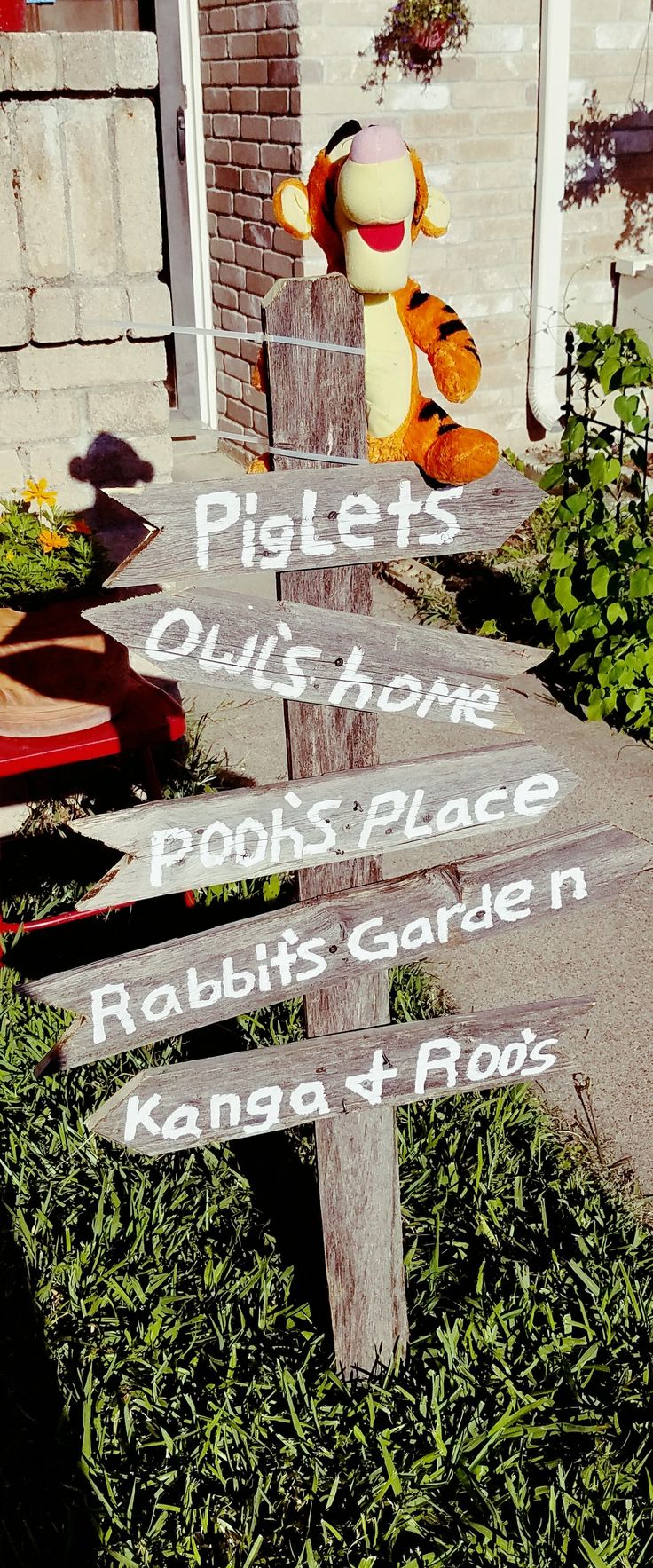 a wooden sign sitting on the side of a road next to a brick building and green grass