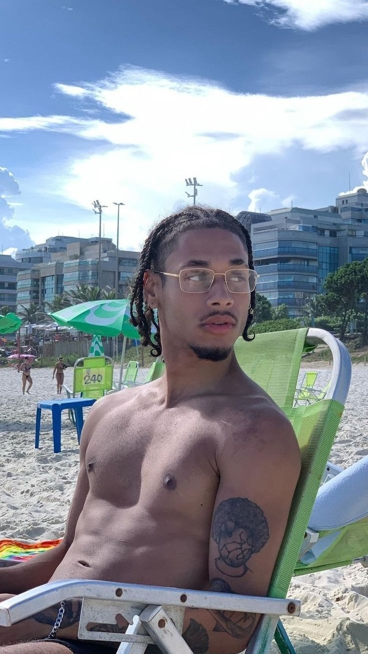 a shirtless man sitting in a lawn chair on the beach with his arm crossed