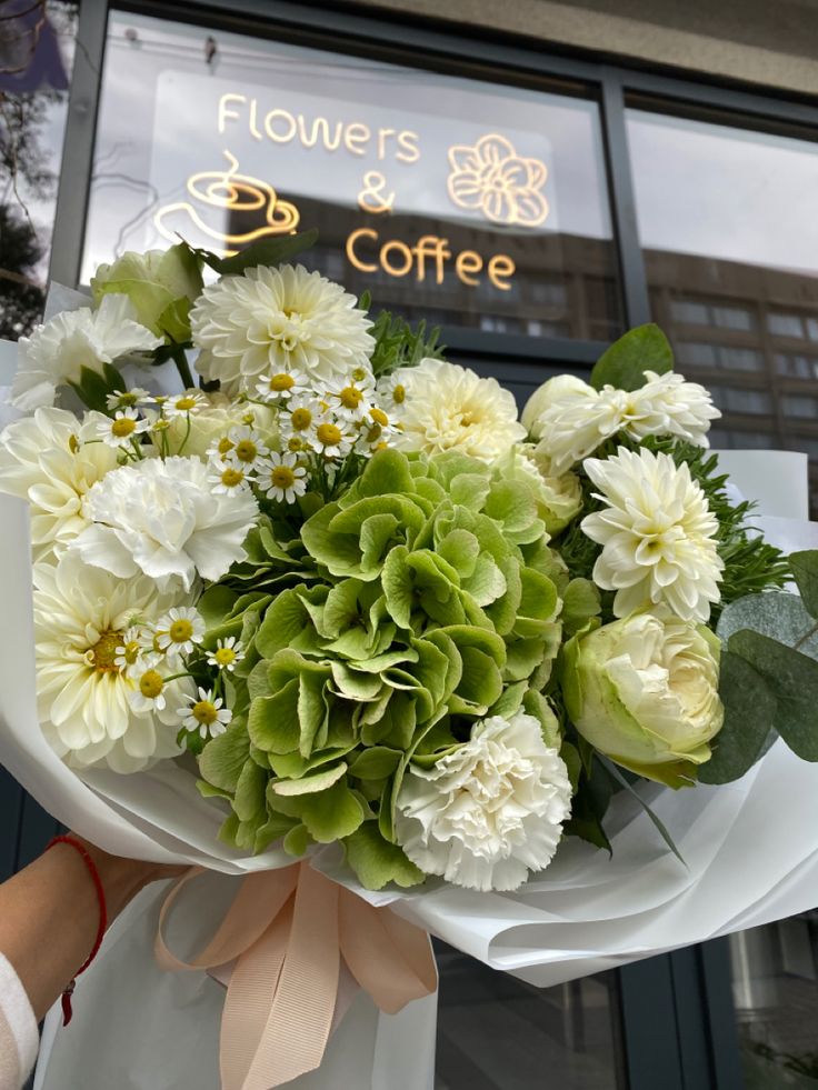 a bouquet of white and green flowers in front of a coffee shop