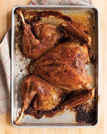 a roasting pan filled with roasted chicken on top of a wooden table next to a napkin