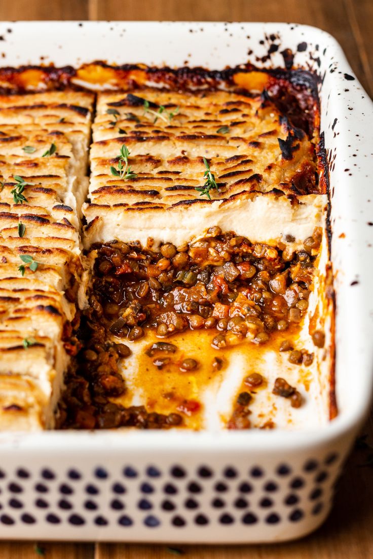 a casserole dish with meat, cheese and sauce in it on a wooden table