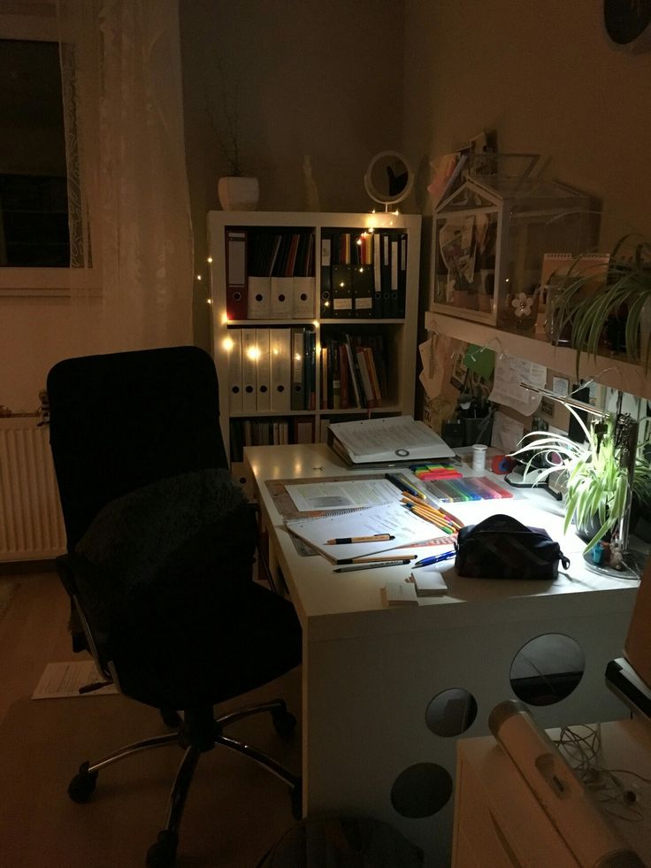 a desk with some books and papers on it in a room filled with plants, lights and other items