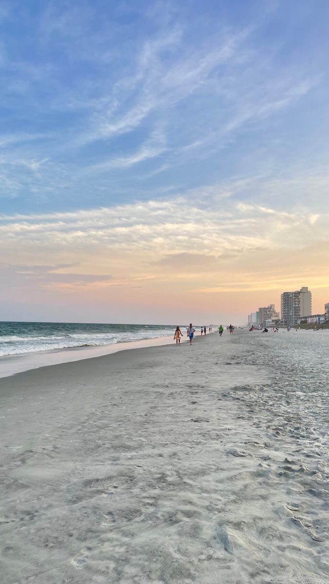 people are walking on the beach at sunset