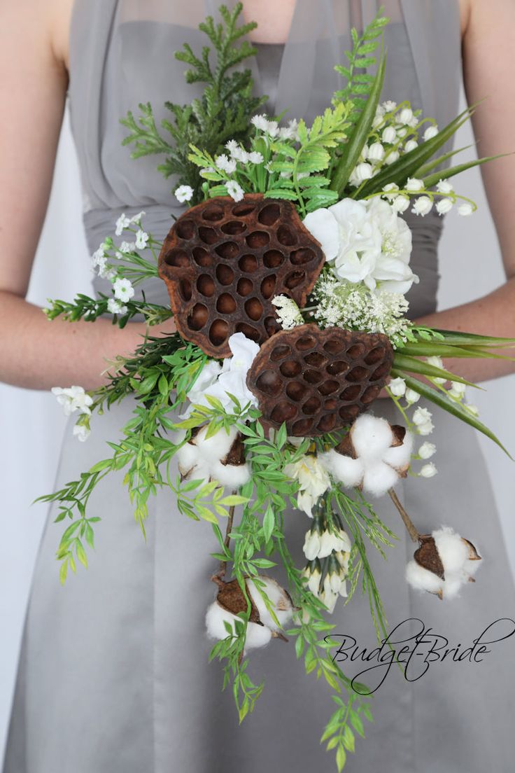 a bridesmaid holding a bouquet of flowers and pine cones in her hands with greenery