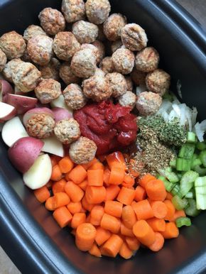 a black bowl filled with meatballs, carrots, celery and onions