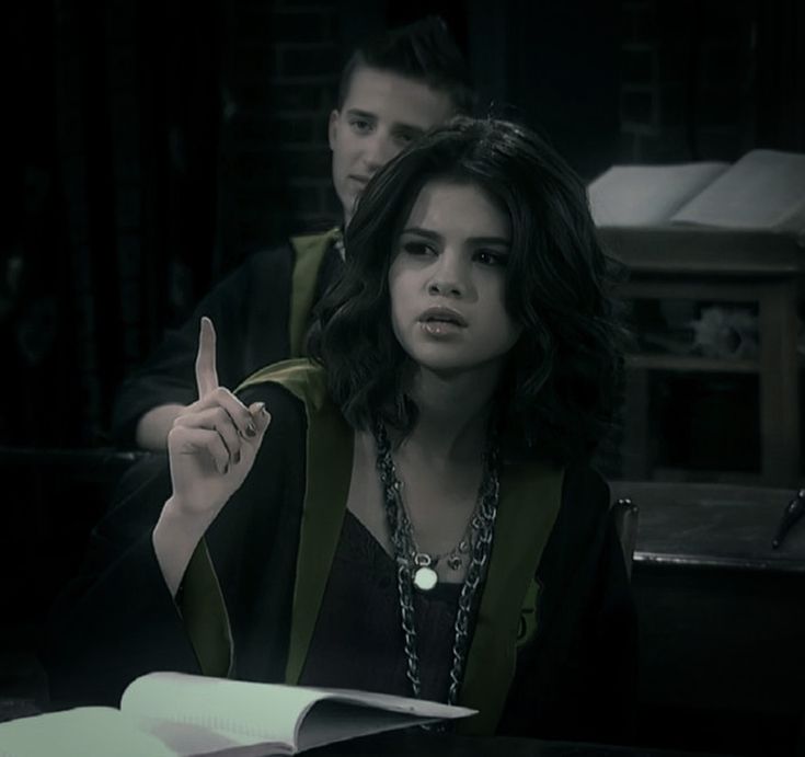 a woman sitting at a table with a book in front of her and another man standing behind her