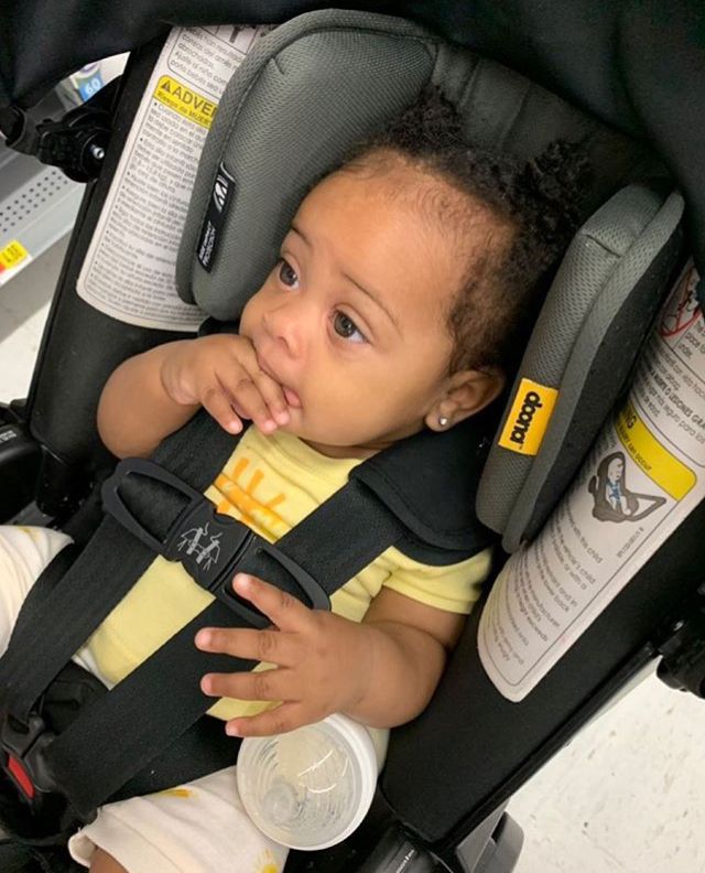 a baby sitting in a car seat with its hand on his chin and looking at the camera