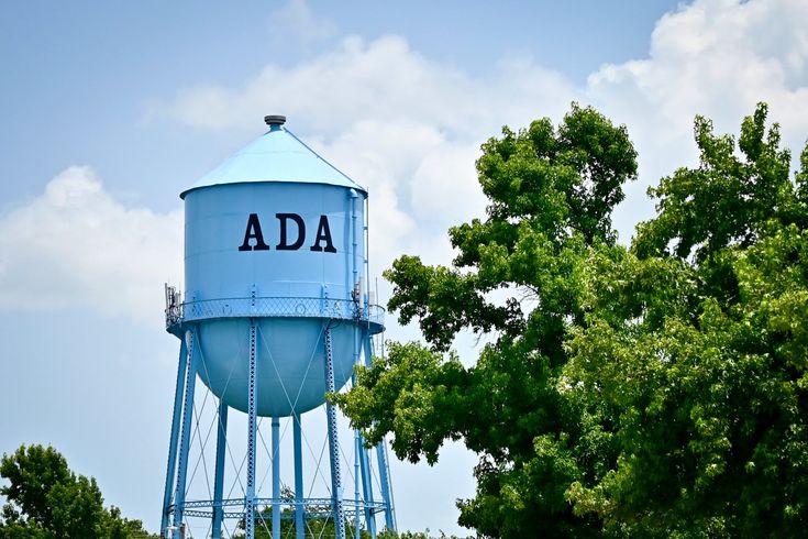 a blue water tower with the word ada on it's side and trees in front