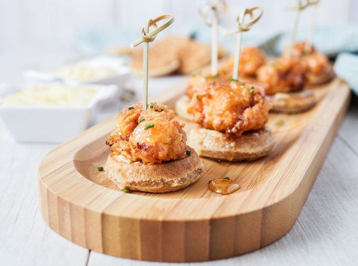 small appetizers with toothpicks are sitting on a wooden tray next to other food