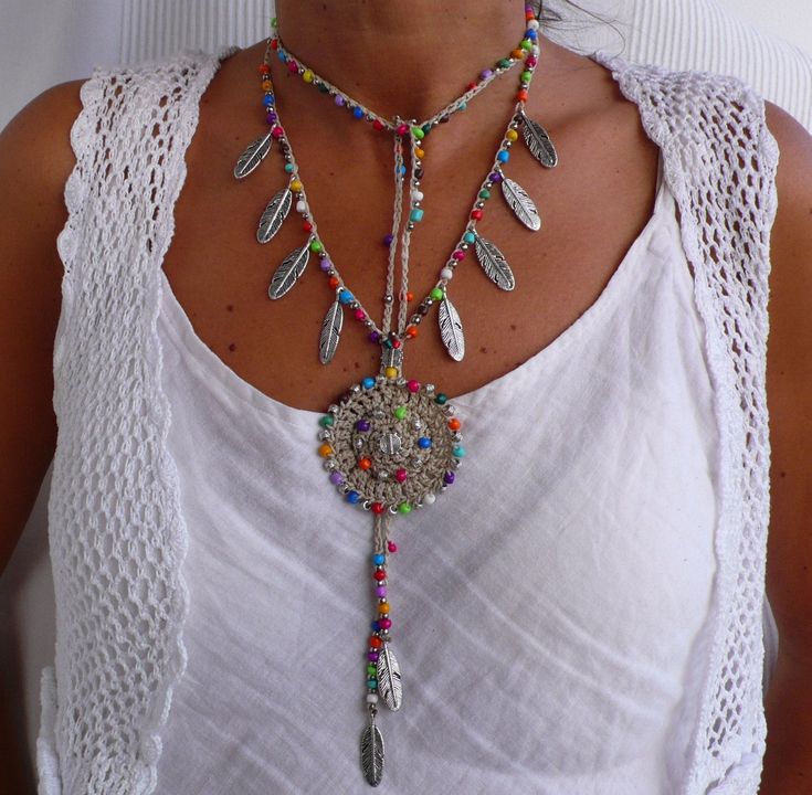 a woman wearing a white tank top and multi colored beaded necklace with feathers on it