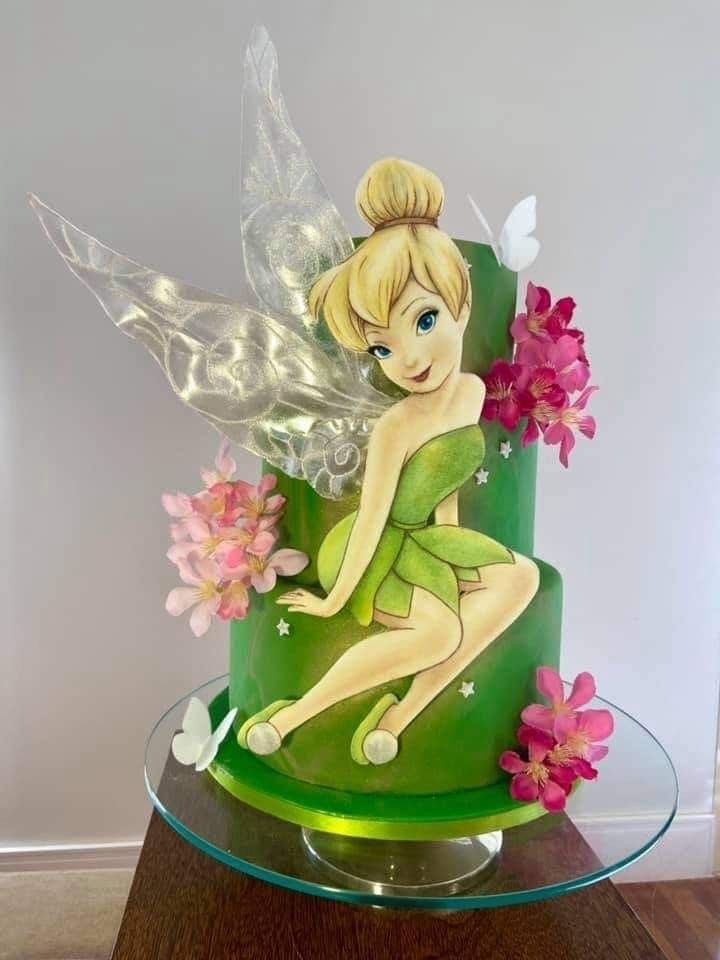 a cake with a tinkerbell sitting on top of it and flowers around the base