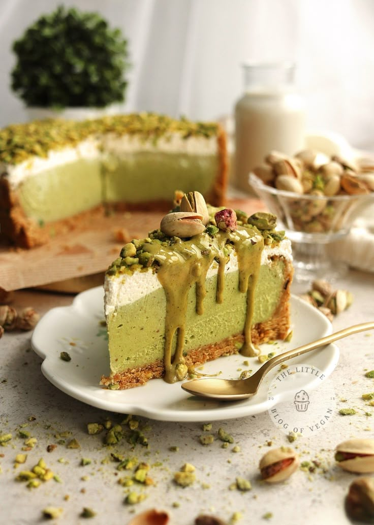 a piece of green cake on a plate with a fork next to it and some nuts in the background