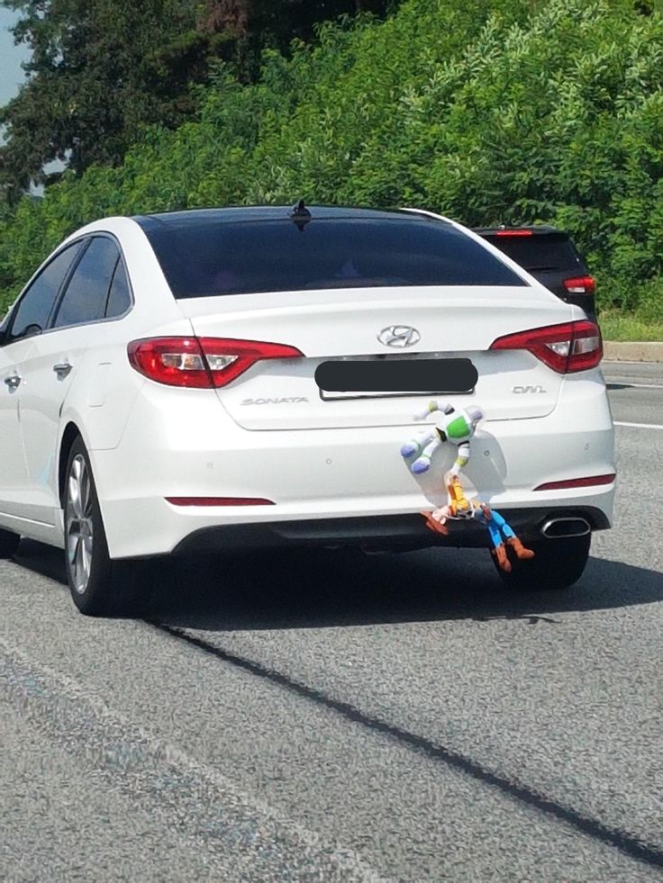 a white car driving down the road with stuffed animals on it's tail end