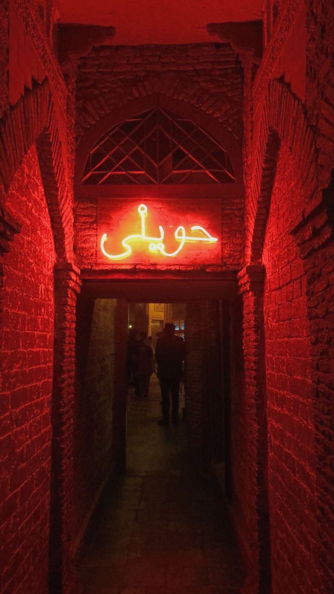 a red neon sign hanging from the side of a brick wall next to a doorway