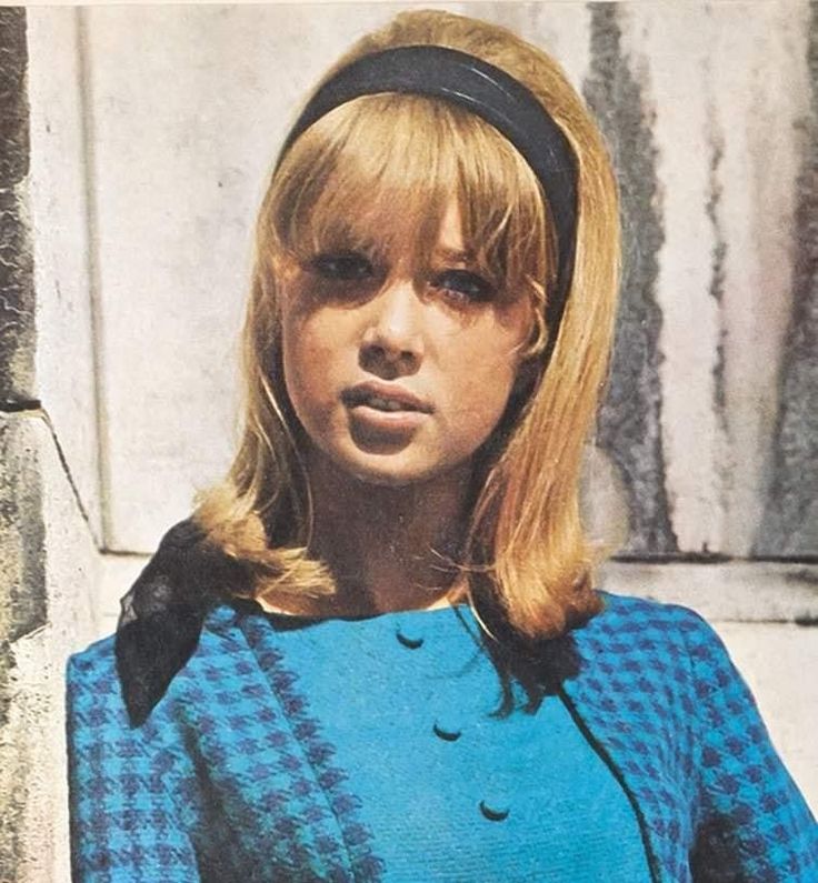 a woman with blonde hair wearing a blue dress and black headband standing in front of a wall