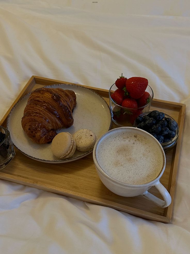 a breakfast tray with coffee, fruit and croissants on the bed in front of it