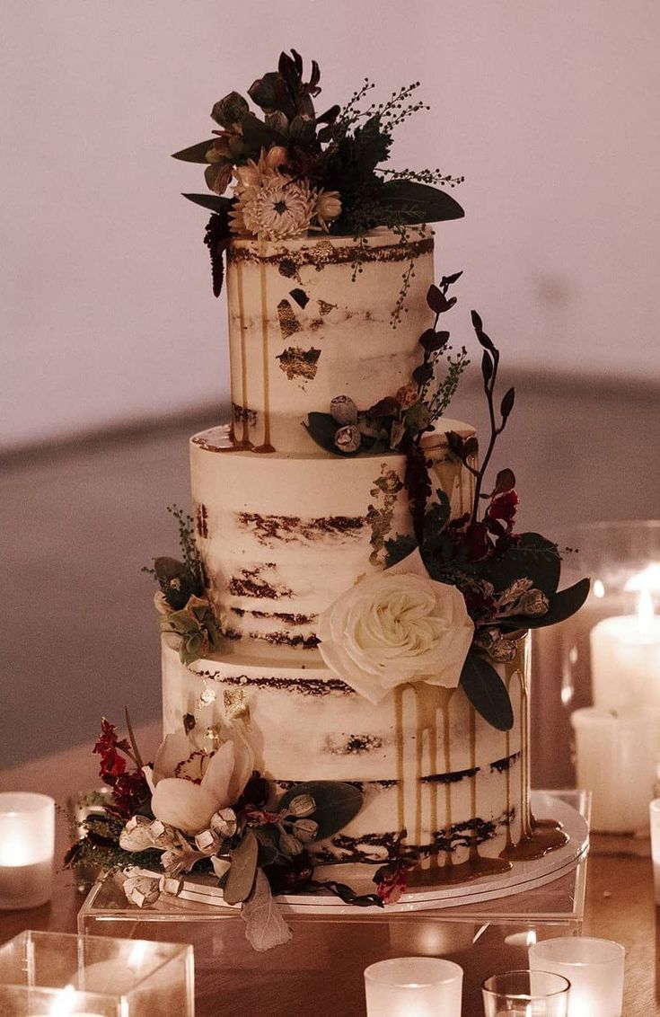 a three tiered cake with flowers and candles around it on a table in front of lit candles