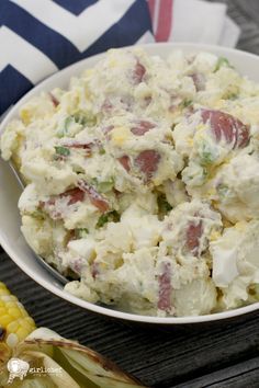 a white bowl filled with potato salad next to an ear of corn