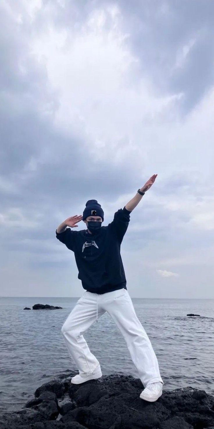 a man standing on top of a rock next to the ocean with his arms in the air