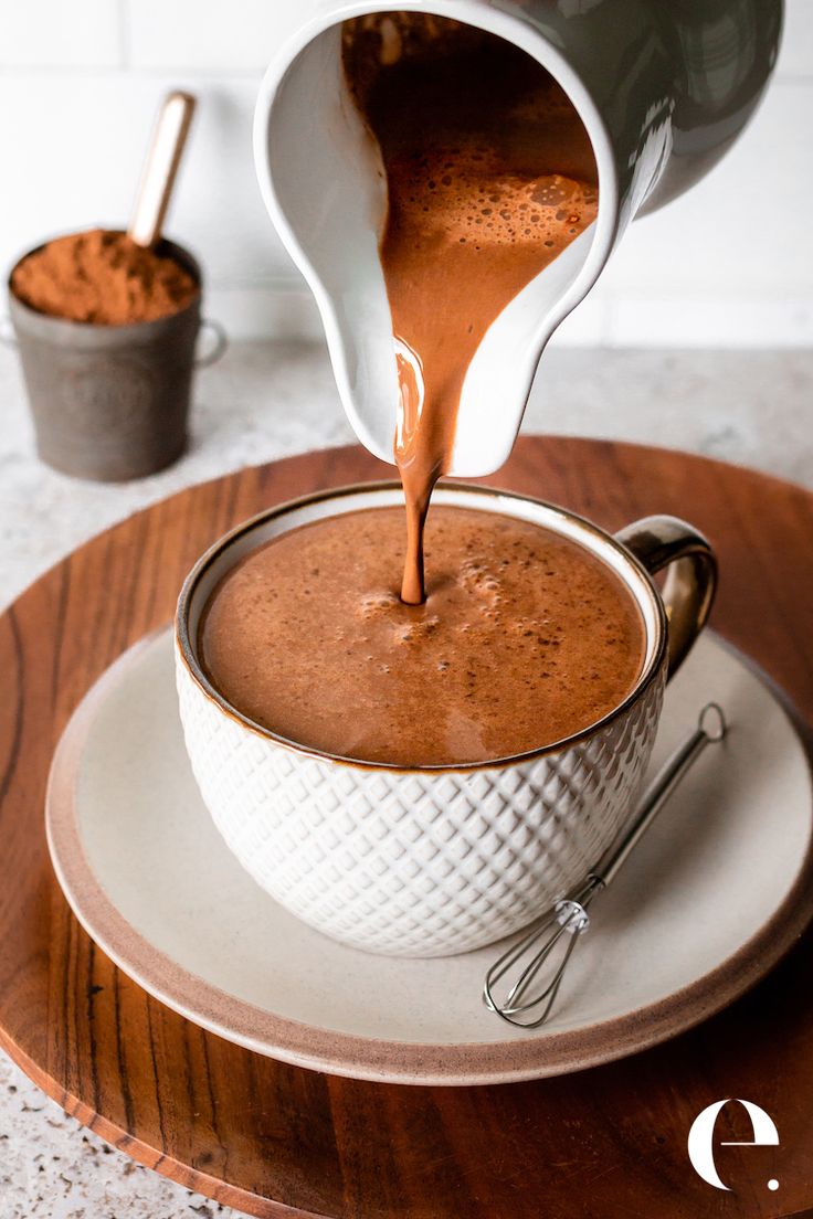 chocolate being poured into a white bowl on top of a wooden plate with spoons