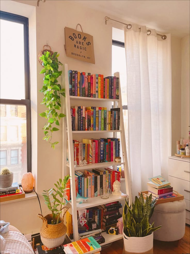 a living room filled with lots of books next to a large window covered in white curtains