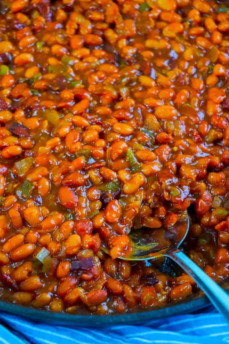 a large pot filled with beans and vegetables on top of a blue cloth next to two spoons