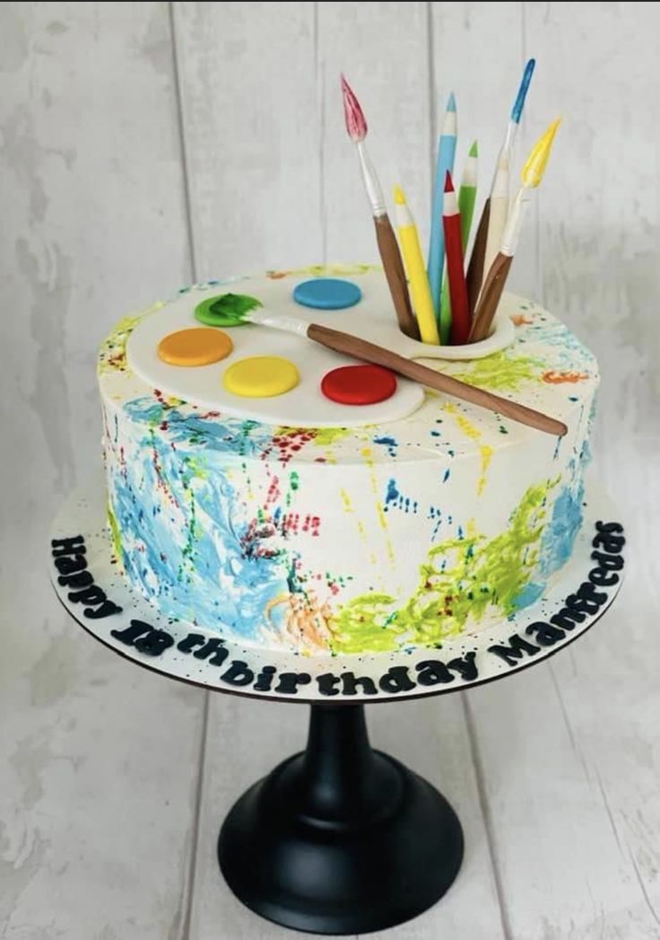 a cake decorated with paint and brushes on top of a black stand in front of a white wall