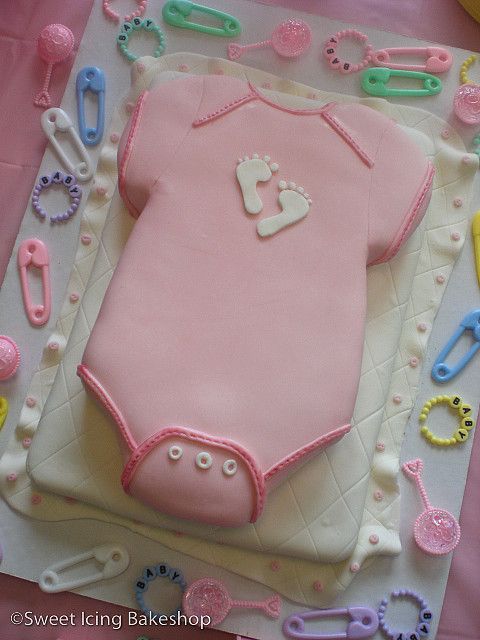 a baby shower cake with pink icing on it's body and accessories around the edges