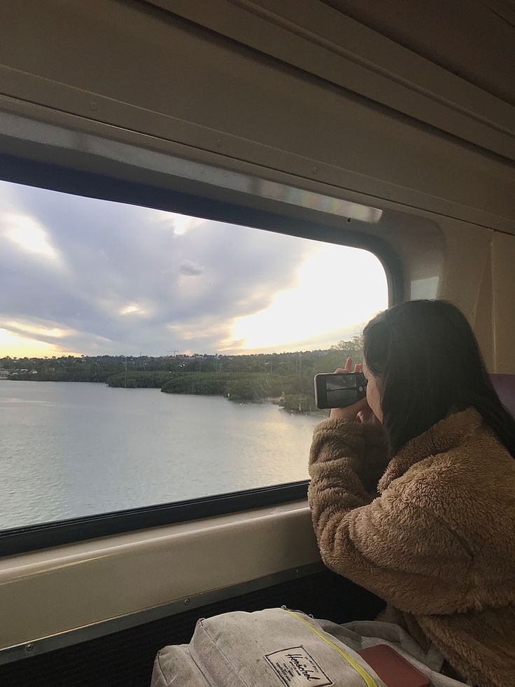 a woman is taking a photo from the inside of a train car looking out at water