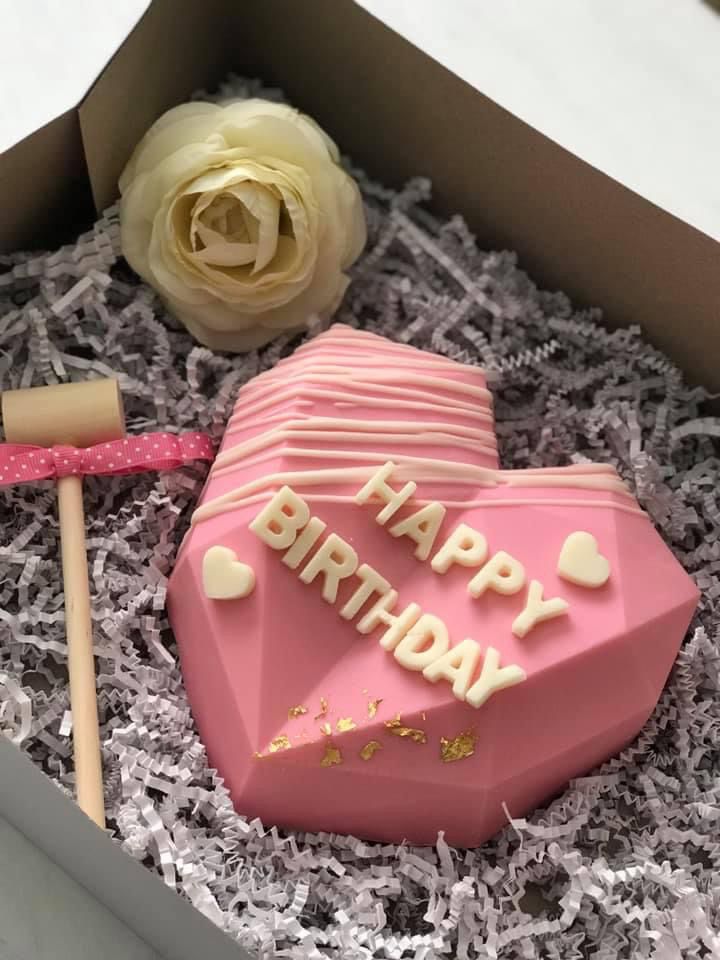 a pink heart shaped cake in a box with a flower on the table next to it