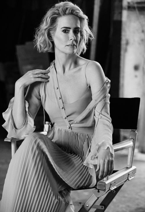 a black and white photo of a woman sitting on a chair with her hands in her pockets