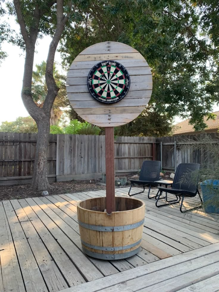 a wooden barrel sitting on top of a wooden deck next to a dart board sign