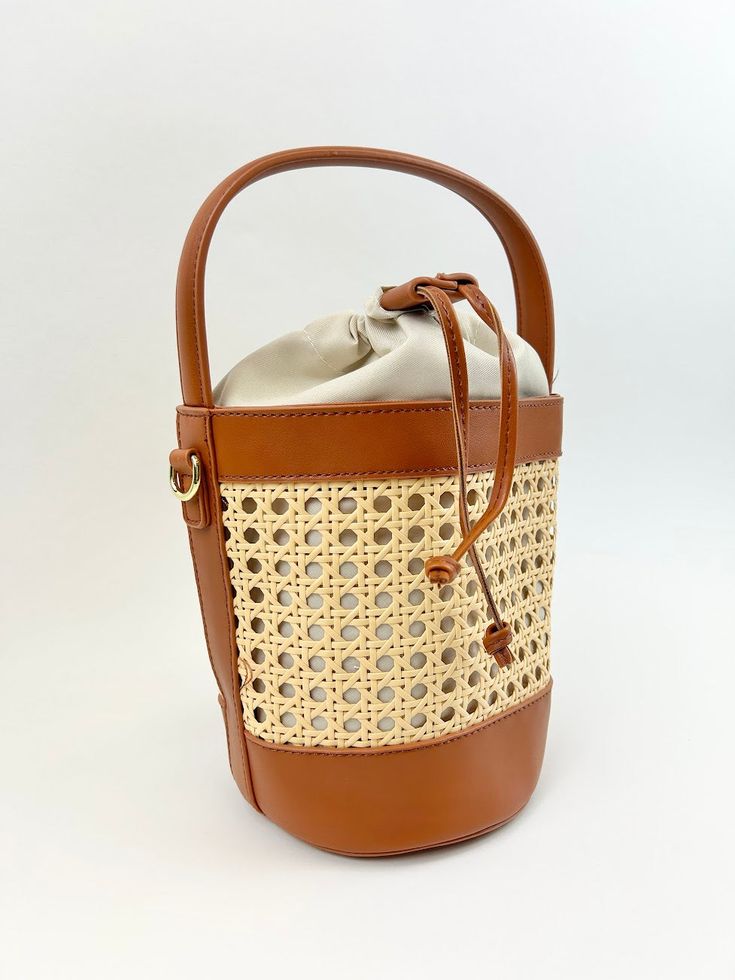 We love a bucket bag to carry all our essentials, and this woven rattan bag is the perfect bag to carry around all summer long! Product Details Material: Vegan Leather & Rattan Size: 11"L x 9"W Handle and Crossbody Strap Features a drawstring closure Brown Crossbody Shoulder Bag With Bamboo Handle, Vacation Woven Leather Pouch Shoulder Bag, Summer Leather Shoulder Bag With Bamboo Handle, Beach Leather Shoulder Bag With Bamboo Handle, Leather Bucket Bag With Bamboo Handle For Daily Use, Chic Brown Woven Leather Bucket Bag, Woven Leather Pouch Shoulder Bag For Vacation, Leather Shoulder Bag With Bamboo Handle For Beach, Chic Leather Bucket Straw Bag