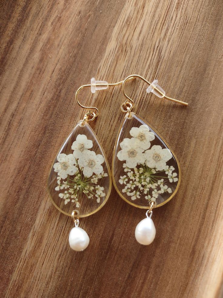 Discover the enchanting allure of our White Floral Earrings with Freshwater Pearls and Real Flowers, exclusively at Sass & Izzy. Each exquisite piece is crafted with hypoallergenic gold plated stainless steel ear wires and 18k gold plated bezels, ensuring both comfort and timeless elegance. Ideal for weddings or a sophisticated everyday look, these earrings encapsulate natural beauty and meticulous craftsmanship. Embrace the fusion of delicate charm and luxurious materials, reflecting Sass & Izzy's commitment to quality and style. Elevate your jewelry collection with a piece that truly stands out. Follow for More! @sassandizzyllc Instagram: www.instagram.com/sassandizzyllc Facebook: www.facebook.com/sassandizzyllc Shop our online store: www.sassandizzyllc.com White Drop Earrings In 14k Gold Filled, White Teardrop 14k Gold Filled Jewelry, White 14k Gold Filled Teardrop Jewelry, White Teardrop 14k Gold Filled Earrings, White 14k Gold-filled Teardrop Earrings, White 14k Gold Filled Teardrop Earrings, Delicate Teardrop Hoop Earrings For Gift, Delicate Teardrop Hoop Earrings As Gift, Delicate Gold Hypoallergenic Earrings