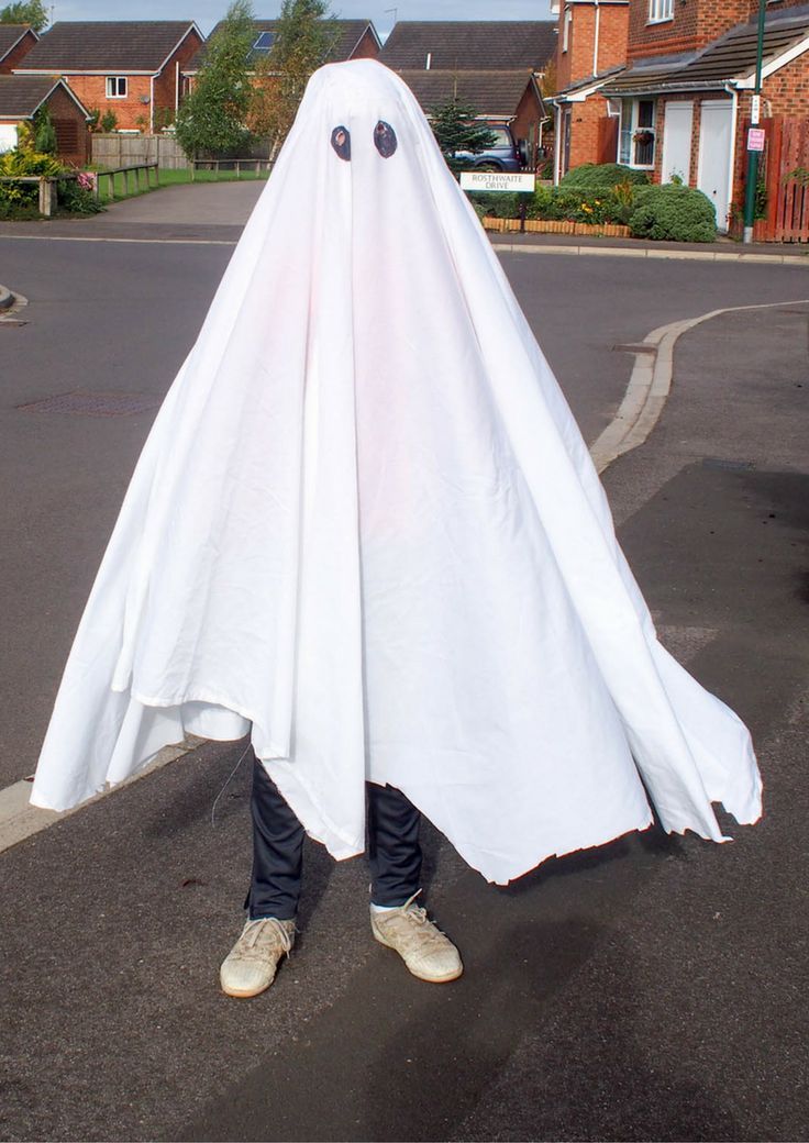 a person wearing a white ghost costume standing in the middle of a street with houses behind them