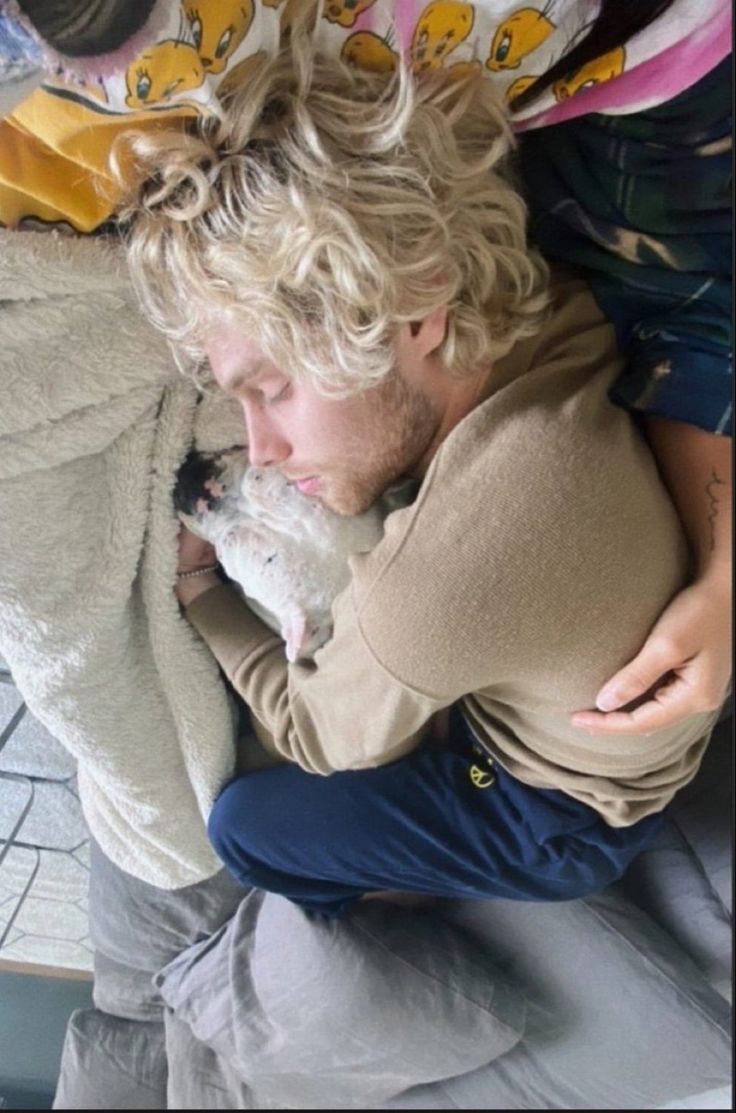 a man with curly hair holding a dog in his lap while sitting on a chair