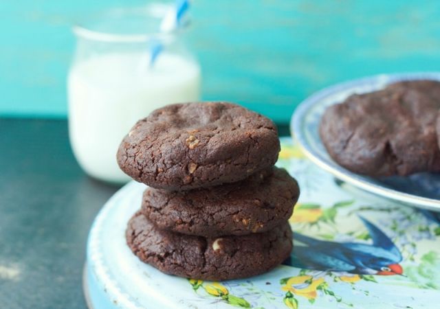 three chocolate cookies on a plate next to a glass of milk